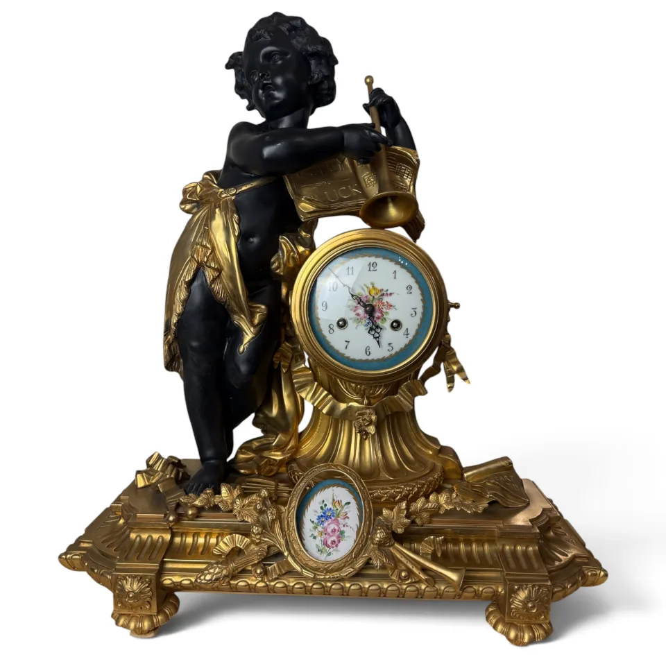 Zegar kominkowy z brązu złoconego i patynowanego na czarno, figura putta z trąbką opartego o nuty z napisem Gluck, porcelanowa tarcza i medalion z malowanymi kwiatami w turkusowej oprawie, cokół z trofeum muzycznym i liśćmi dębu, nóżki z palmetami